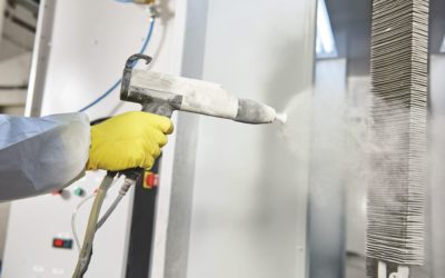 industrial metal coating. Worker man in protective suit with gas mask spraying powder to steel finished parts in painting chamber