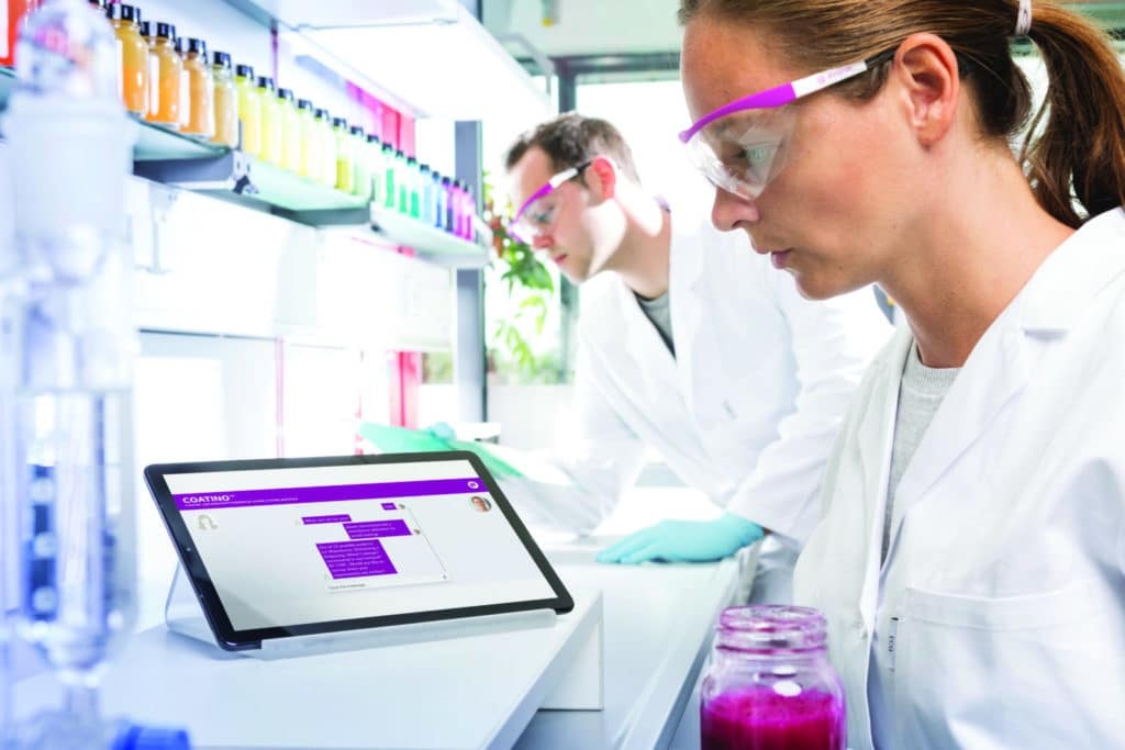 A scientists works in a lab with a tablet open beside her.