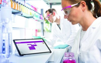 A scientists works in a lab with a tablet open beside her.