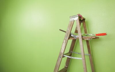 Old antique wooden ladder stands against a half painted green wall with paint roller and tray