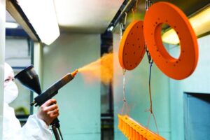 Powder coating of metal parts. A man in a protective suit sprays powder paint from a gun on metal products.