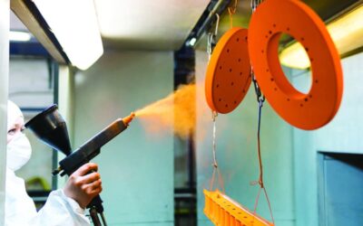 Powder coating of metal parts. A man in a protective suit sprays powder paint from a gun on metal products.