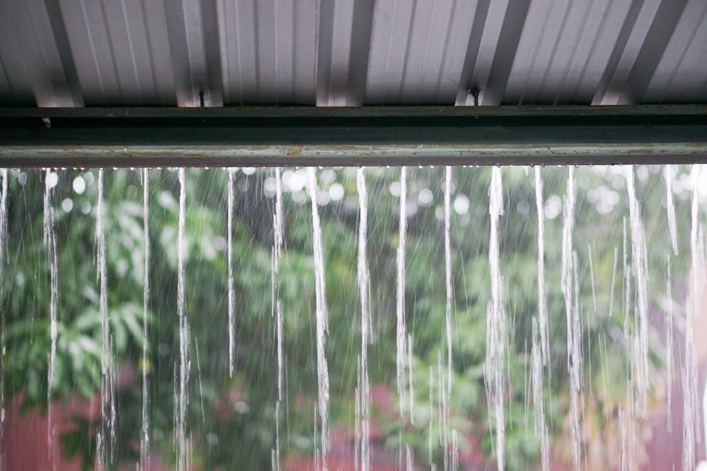 Streams of rain water pour off a corrugated roof