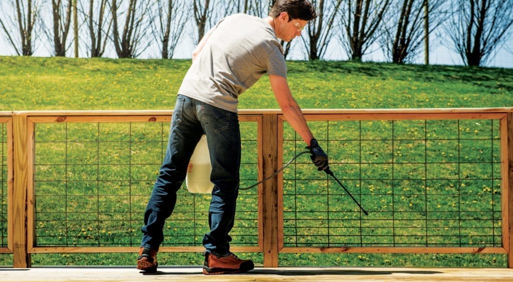 man spraying wood deck with preservative