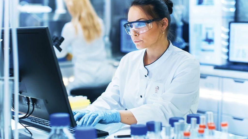 Medical Research Scientist Typing Information Obtained from New Experimental Drug Trial. She Works in a Bright and Modern Laboratory.