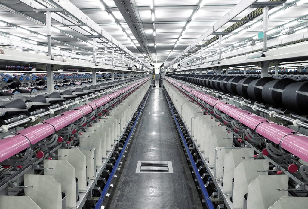 Manufacturing plant aisle shown with fluorescent lights and a concrete floor.