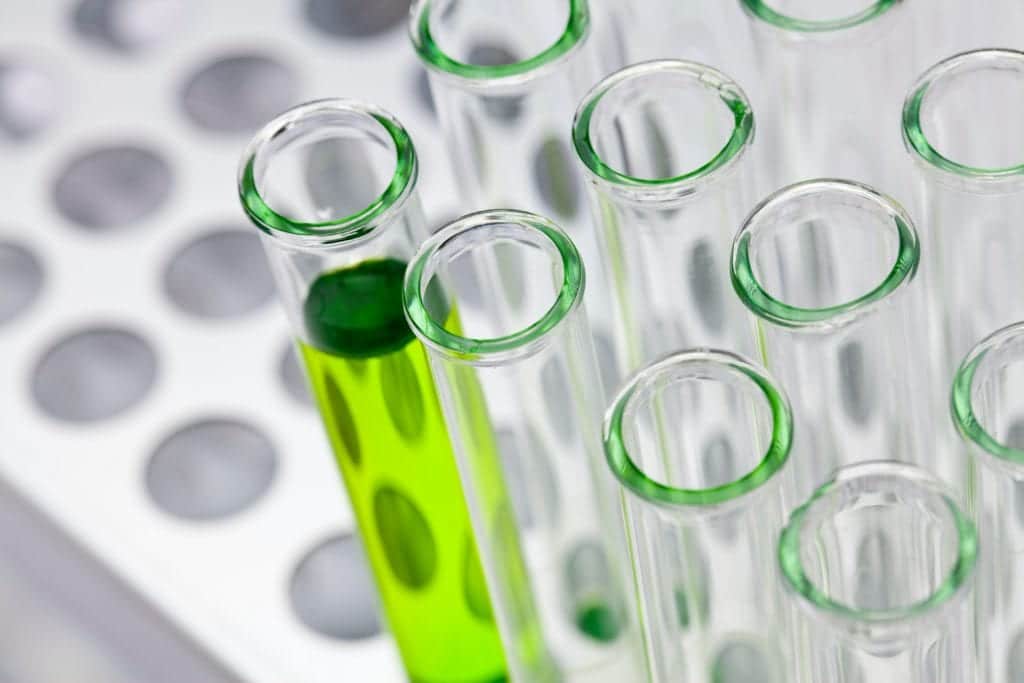 Test tubes sit in a tray, one has a neon green liquid.