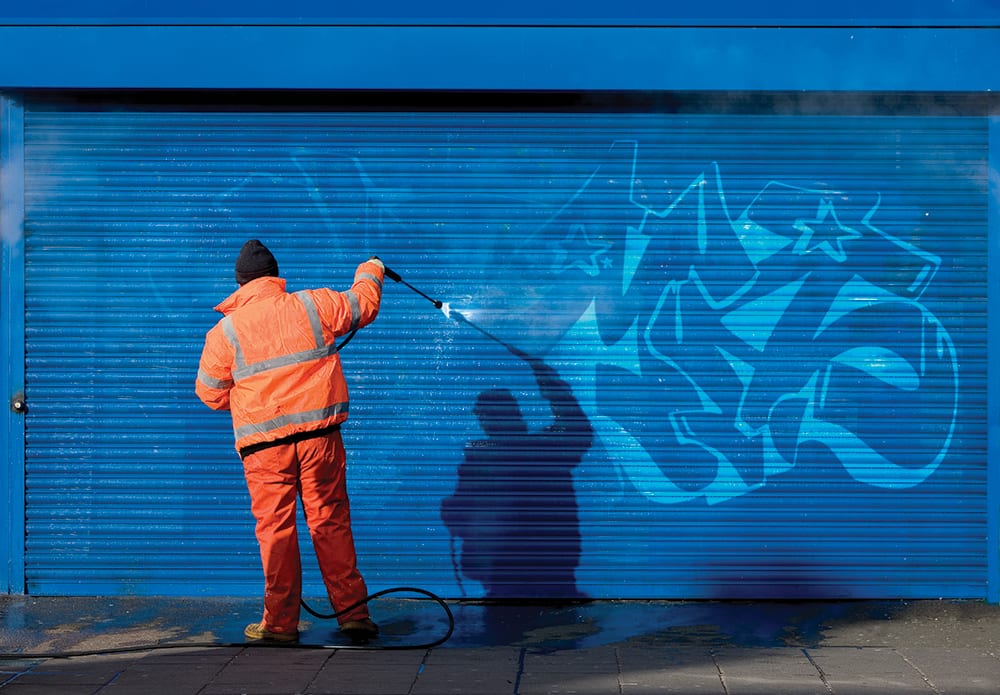 Washing graffiti off a security grill.