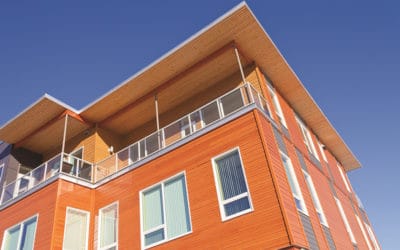 Upper storey detail of timber clad apartment building painted bright with penthouse balcony under blue sky