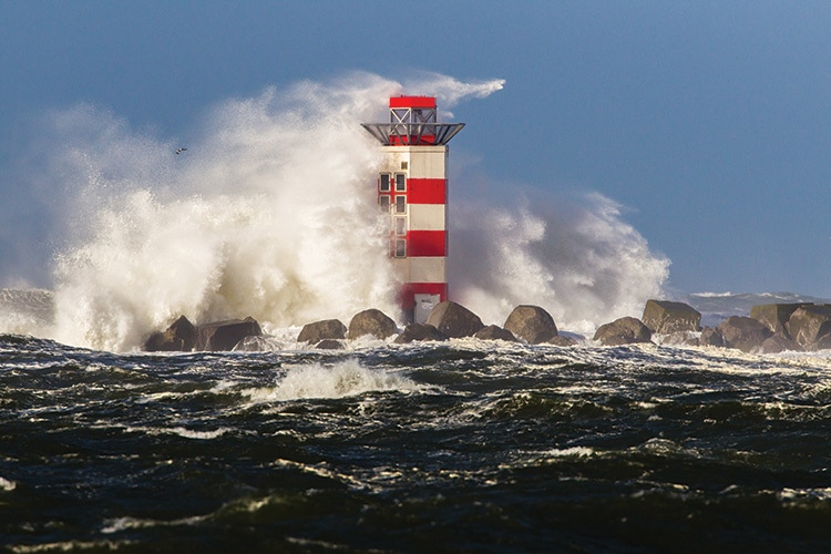 Big waves crashing against the lighthouse at the tip of the pier of Ijmuiden, Netherlands, during severe storm over the North Sea.