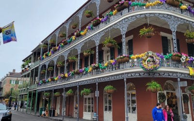 A New Orleans building with three stories is decorated with yellow, purple, and green flowers for Mardi Gras.