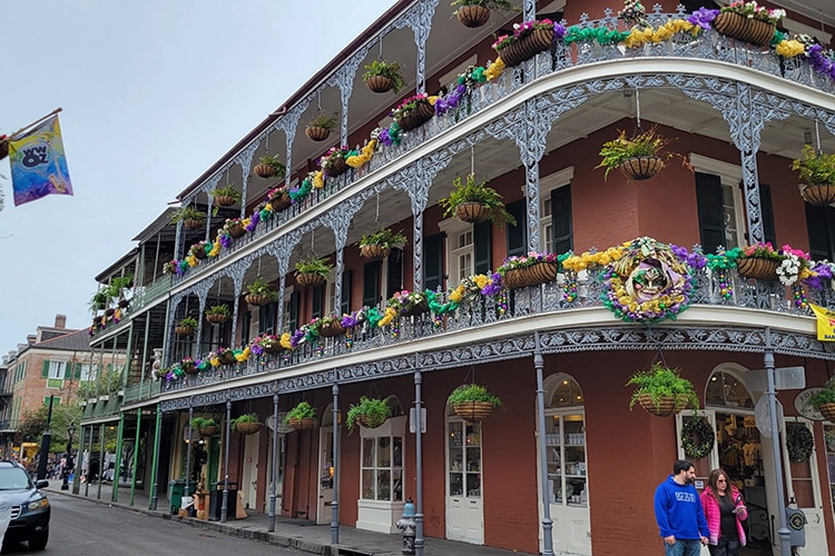 A New Orleans building with three stories is decorated with yellow, purple, and green flowers for Mardi Gras.