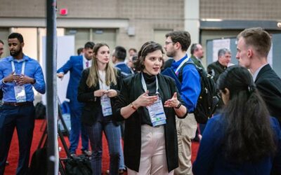 AMPP Conference attendees wearing lanyards stand and talk with others in a large room.
