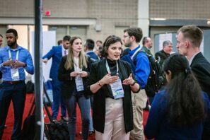 AMPP Conference attendees wearing lanyards stand and talk with others in a large room.