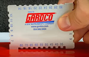 Person holds up a white piece of plastic with ridges around it and corresponding measurements. The Gardco logo appears in the center.