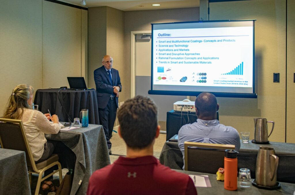 A man speaking before a room of conference attendees